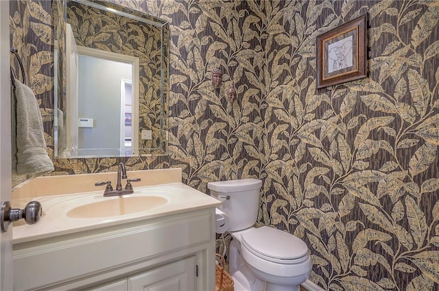 bathroom featuring toilet, vanity, and wallpapered walls