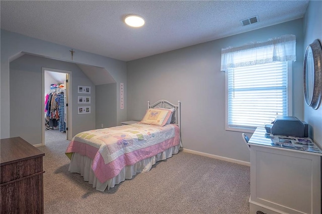 bedroom with light carpet, visible vents, a spacious closet, and a textured ceiling