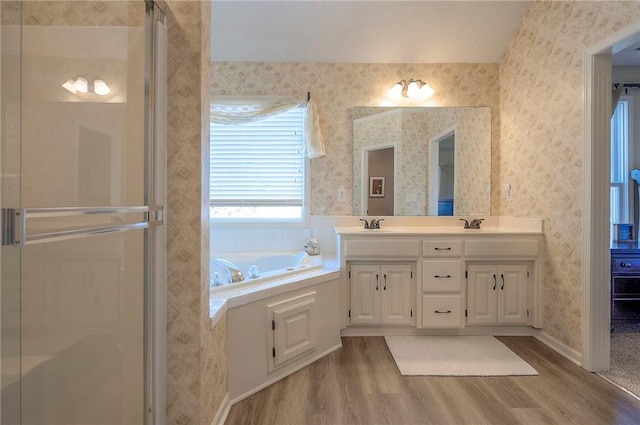 full bath featuring a shower stall, wallpapered walls, a garden tub, double vanity, and wood finished floors