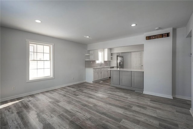 kitchen with stainless steel refrigerator with ice dispenser, open shelves, light countertops, wood finished floors, and baseboards