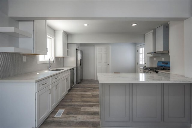 kitchen featuring a peninsula, wall chimney range hood, open shelves, and a sink