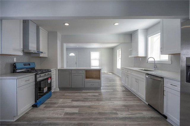 kitchen with light wood-style flooring, a sink, a peninsula, appliances with stainless steel finishes, and wall chimney exhaust hood