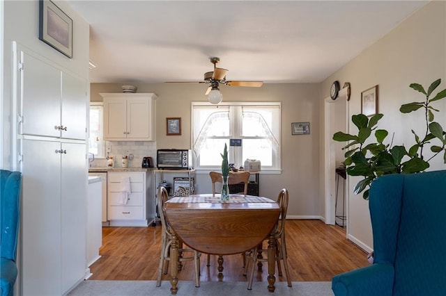 dining room featuring a ceiling fan, a toaster, wood finished floors, and baseboards