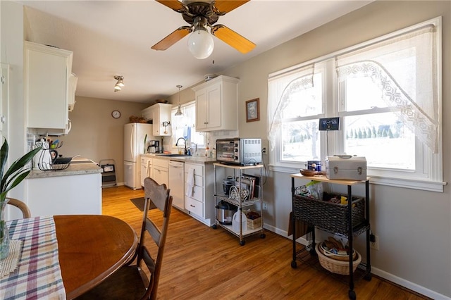 kitchen with white appliances, white cabinetry, light wood-style floors, and a sink