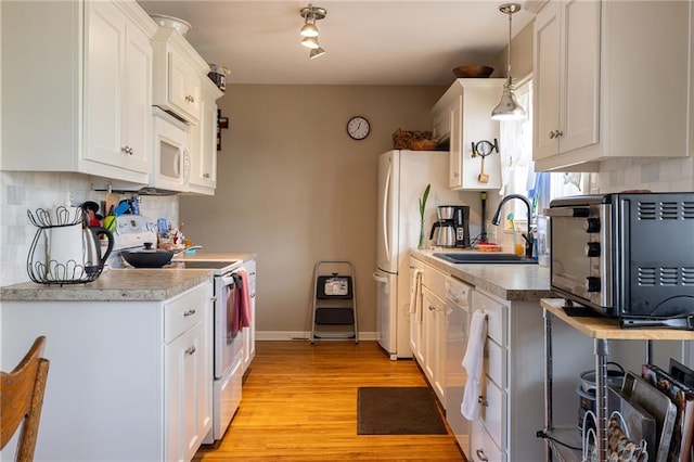 kitchen featuring white appliances, a sink, white cabinets, light wood-style floors, and tasteful backsplash