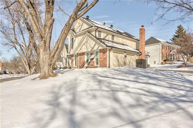 snow covered property with a garage and brick siding