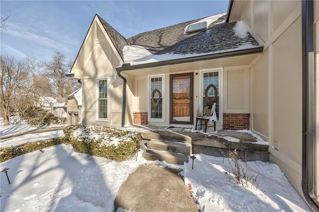 snow covered property entrance featuring roof with shingles and brick siding