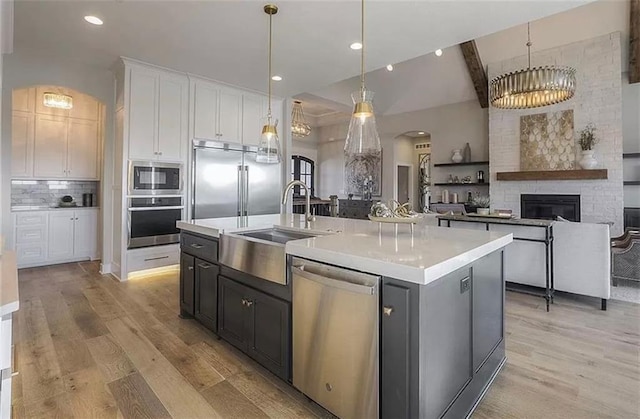 kitchen with arched walkways, a sink, white cabinets, built in appliances, and a large fireplace