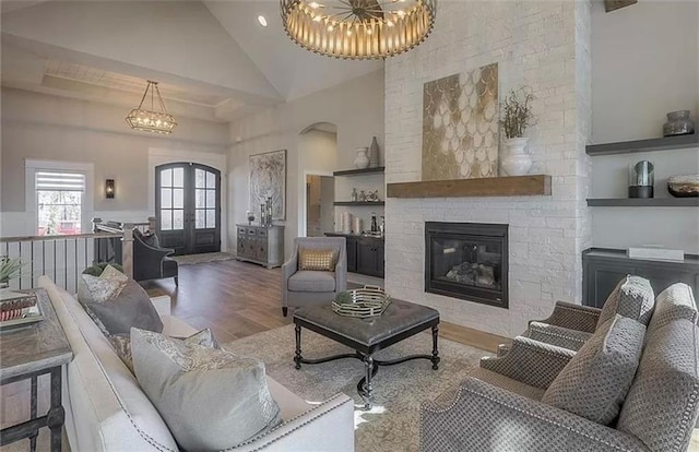 living area featuring wood finished floors, high vaulted ceiling, a fireplace, french doors, and a chandelier