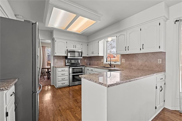 kitchen featuring a peninsula, white cabinetry, stainless steel appliances, and a sink