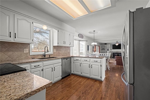 kitchen featuring a peninsula, dark wood-style flooring, a sink, white cabinets, and appliances with stainless steel finishes