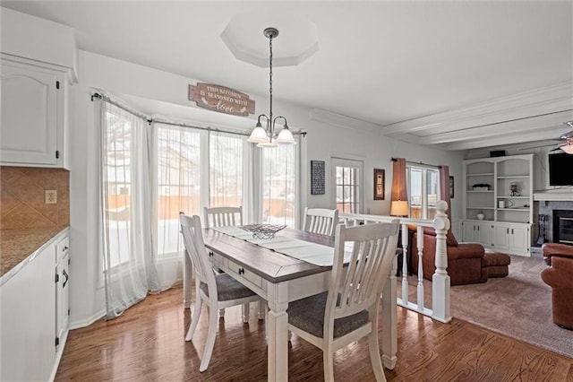 dining room with light wood-type flooring, ceiling fan with notable chandelier, and a glass covered fireplace