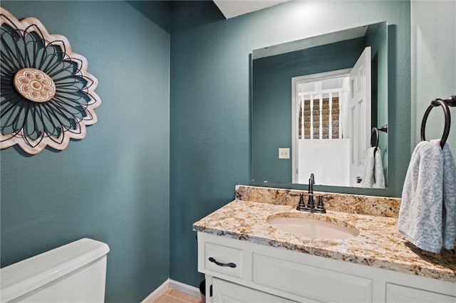 half bathroom featuring a textured wall, vanity, toilet, and baseboards