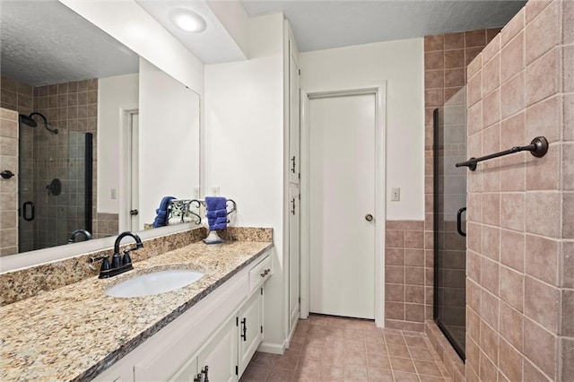 full bath with tile patterned floors, a shower stall, a textured ceiling, and vanity