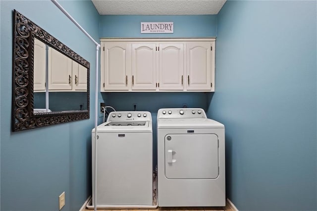 clothes washing area with cabinet space, washing machine and dryer, baseboards, and a textured ceiling