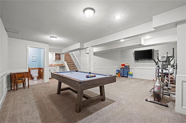 recreation room with a textured ceiling, wainscoting, carpet flooring, and a decorative wall