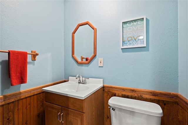 bathroom featuring toilet, a wainscoted wall, wooden walls, and vanity