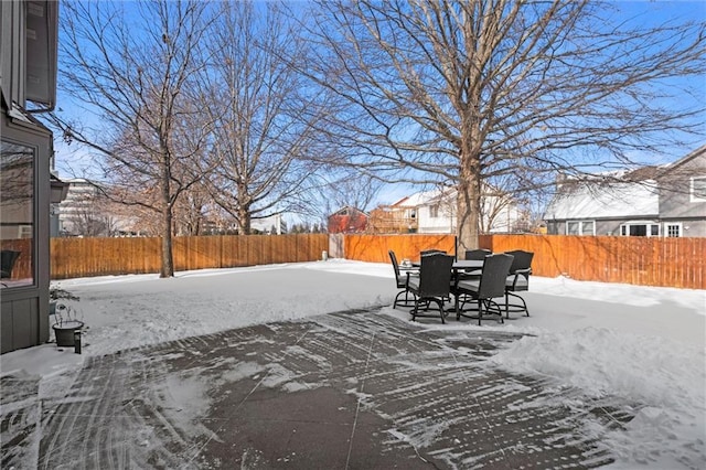 snowy yard with outdoor dining area, a fenced backyard, and a patio