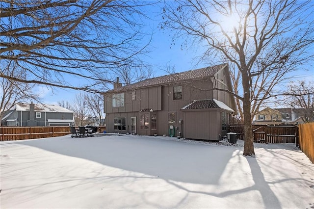 snow covered house with a chimney and fence private yard