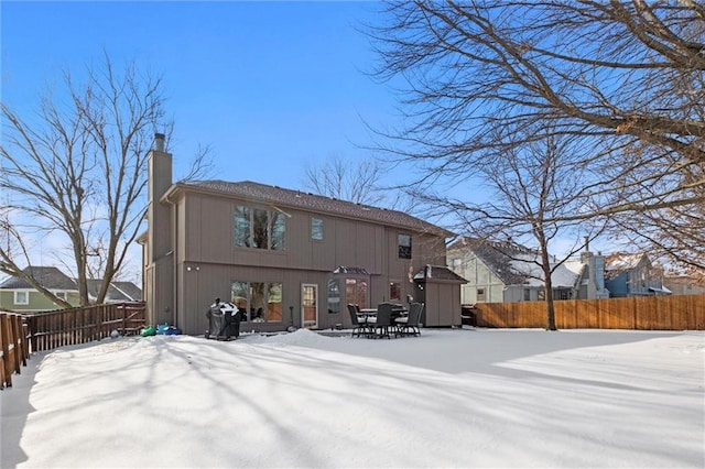 snow covered property featuring a fenced backyard, a chimney, and an outdoor structure