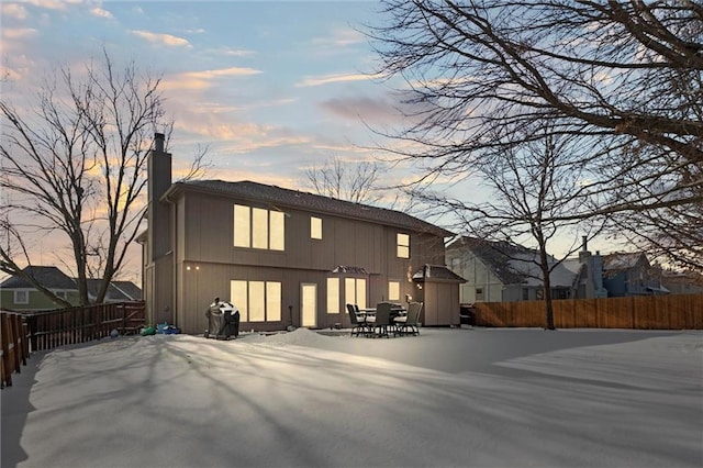 back of property at dusk featuring a patio, a chimney, and fence