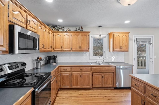 kitchen with brown cabinets, stainless steel appliances, hanging light fixtures, light wood-style floors, and a sink