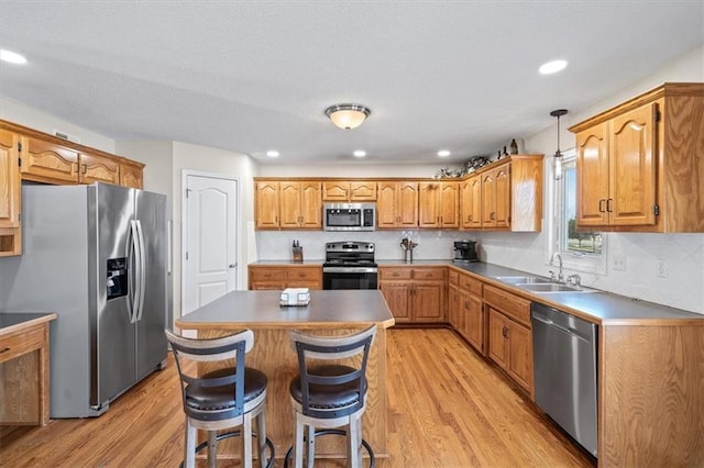 kitchen featuring appliances with stainless steel finishes, decorative light fixtures, a center island, light wood-type flooring, and a sink