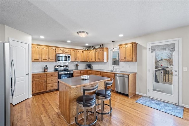 kitchen with a center island, appliances with stainless steel finishes, a sink, light wood-type flooring, and a kitchen bar