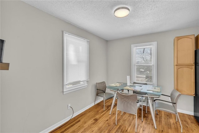 dining area featuring a textured ceiling, light wood-type flooring, and baseboards