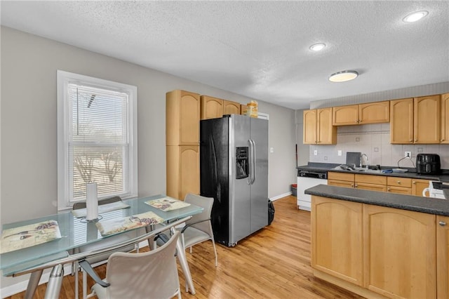 kitchen with light brown cabinets, a sink, dishwasher, dark countertops, and stainless steel fridge