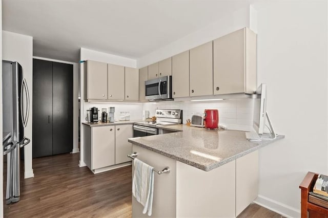 kitchen featuring backsplash, a peninsula, dark wood-style floors, cream cabinetry, and stainless steel appliances