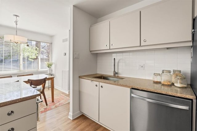 kitchen with light stone countertops, a sink, decorative backsplash, light wood-style floors, and dishwasher