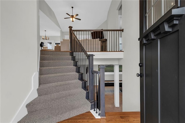 staircase with ceiling fan with notable chandelier, high vaulted ceiling, and wood finished floors