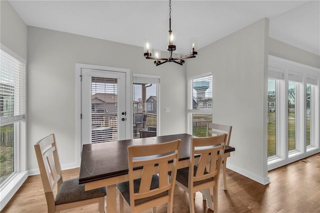 dining room featuring a notable chandelier, baseboards, wood finished floors, and a healthy amount of sunlight