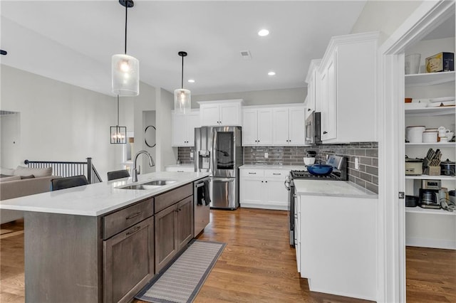 kitchen with appliances with stainless steel finishes, white cabinets, a sink, and wood finished floors