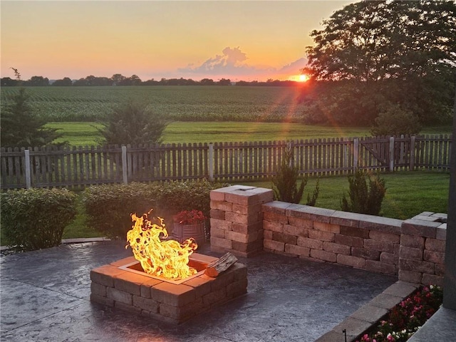 patio terrace at dusk with a fenced backyard, a fire pit, and a rural view