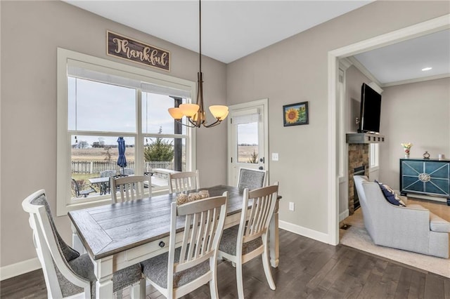 dining room with dark wood-style floors, baseboards, a notable chandelier, and a stone fireplace