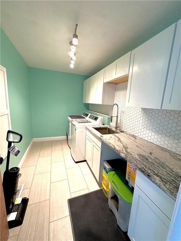 kitchen with tasteful backsplash, independent washer and dryer, white cabinets, and a sink