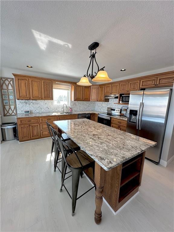 kitchen with brown cabinetry, a center island, stainless steel appliances, under cabinet range hood, and a sink