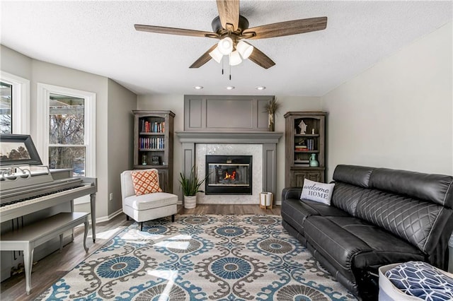 living area with dark wood-style floors, a premium fireplace, a textured ceiling, and a ceiling fan