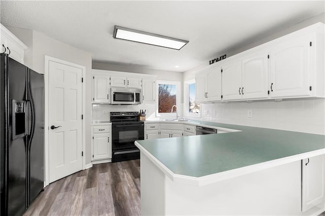 kitchen with a peninsula, black appliances, white cabinets, and a sink