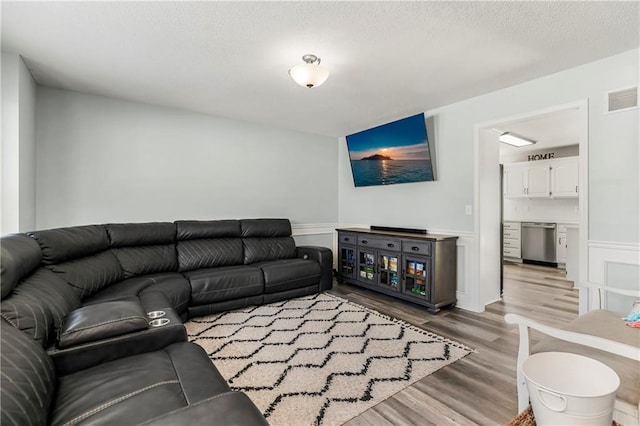 living area featuring light wood-type flooring, visible vents, a textured ceiling, and wainscoting