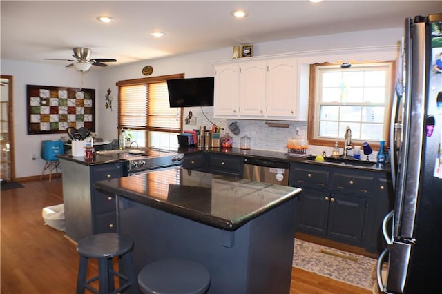 kitchen featuring a sink, a kitchen island, white cabinets, appliances with stainless steel finishes, and dark countertops