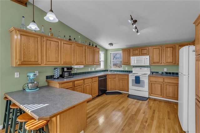 kitchen featuring vaulted ceiling, a sink, white appliances, a peninsula, and a kitchen breakfast bar