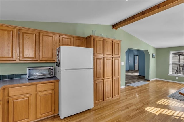 kitchen with arched walkways, a toaster, light wood-style flooring, lofted ceiling with beams, and freestanding refrigerator