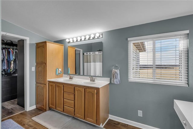 bathroom featuring double vanity, wood finished floors, a sink, and baseboards