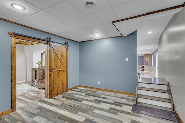 below grade area with a paneled ceiling, visible vents, a barn door, wood finished floors, and baseboards