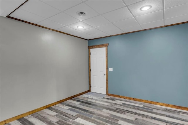 empty room with baseboards, visible vents, a drop ceiling, ornamental molding, and wood finished floors