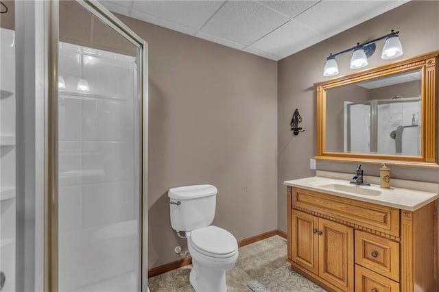 bathroom featuring baseboards, a drop ceiling, toilet, vanity, and a shower stall