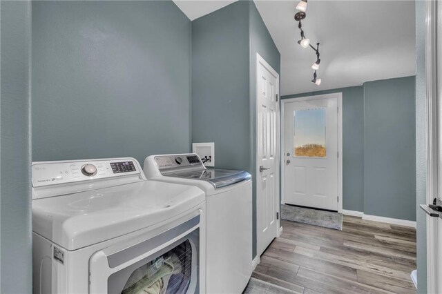 clothes washing area featuring laundry area, baseboards, washer and clothes dryer, wood finished floors, and track lighting